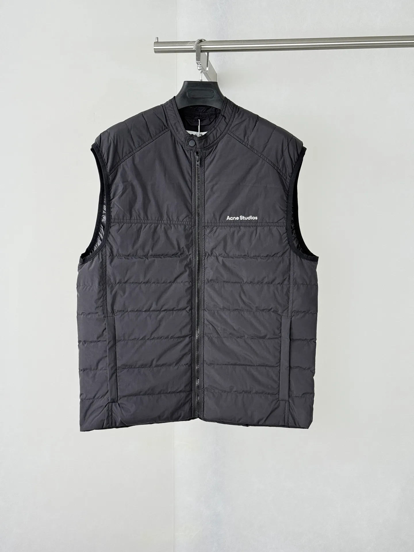 Acne Studio Rib Stand Collar Padded Vest Jacket is made of micro-wrinkled nylon fabric of the same specifications as the original version, with horizontal cotton quilting technology. The spacing and width of each quilting line are strictly reproduced, and the cotton is evenly filled and will not clump and run away. The simple white letters are printed on the chest, and the font weight, size, and body positioning are repeatedly adjusted and matched. The printing is delicate and soft, with no glue feel. The stand-up collar structure, collar snap button + main zipper combination, split panels in the middle of the back, raglan seams, and cuff hemming are all 1:1 restoration of the original craftsmanship Size: S/M/L/XL